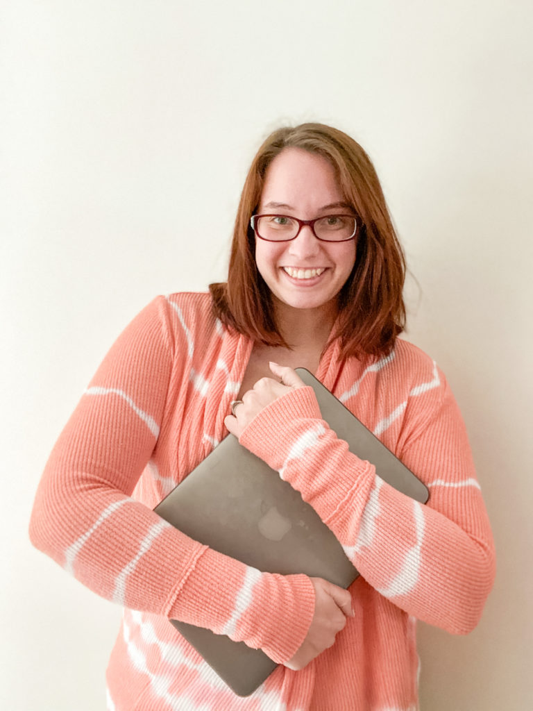 Blog writer holds laptop computer in pink sweater
